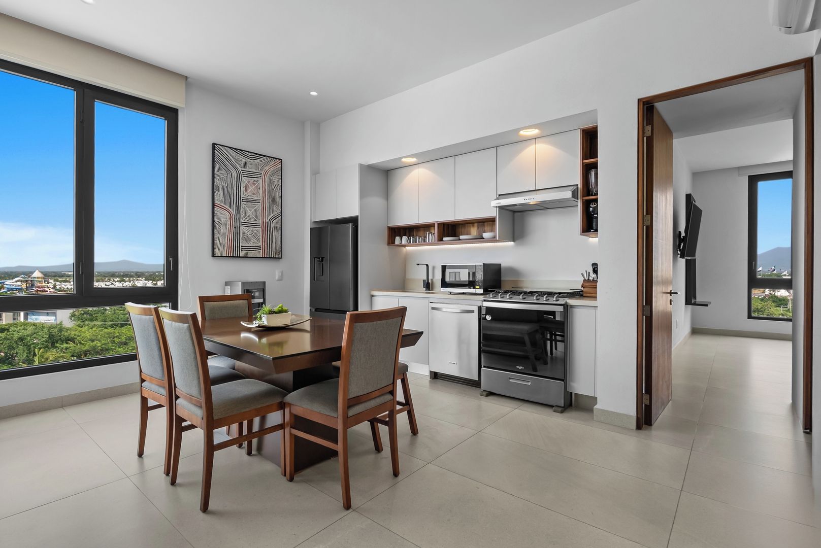 A modern kitchen with a dining area, large windows, and a view of the city.