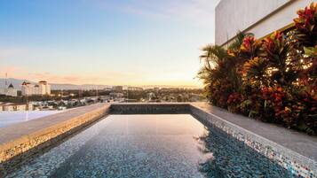 A rooftop infinity pool with a view of a cityscape at sunset.