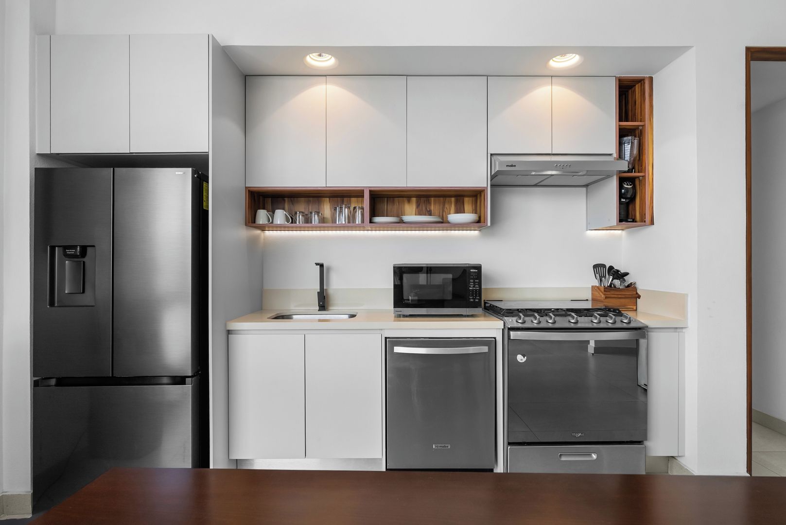A modern kitchen with stainless steel appliances, a microwave, and wooden shelves.