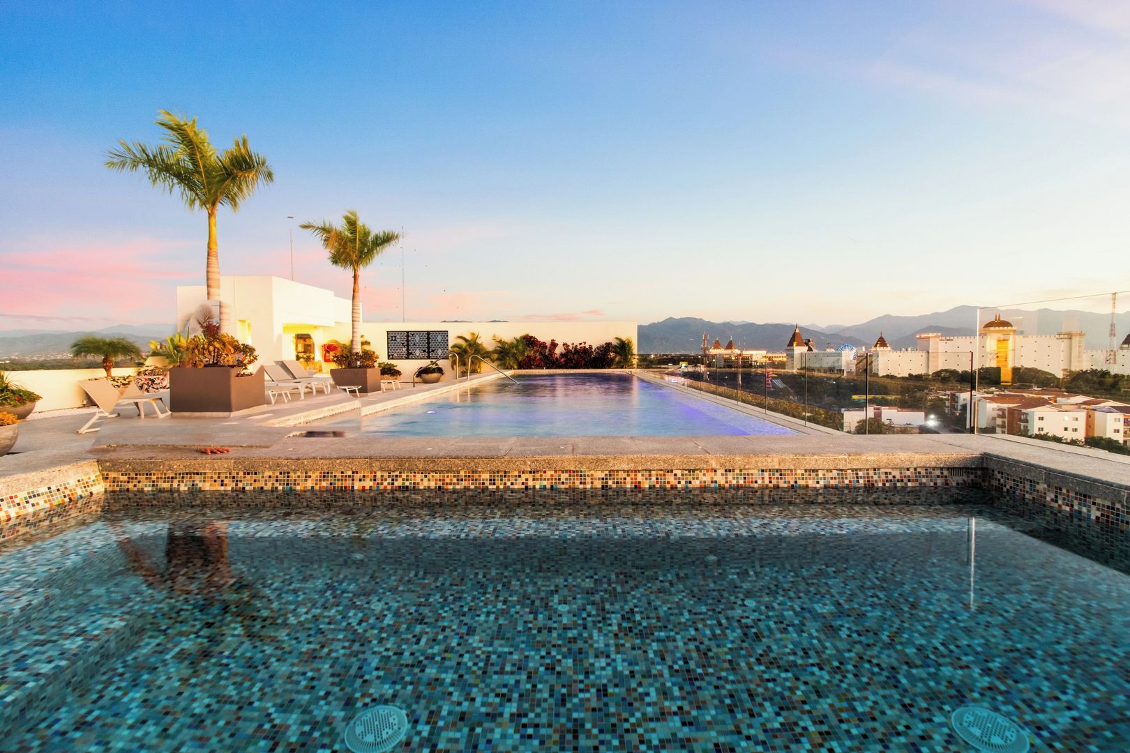 A swimming pool with a tiled edge, surrounded by lounge chairs and palm trees.
