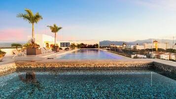 A swimming pool with a tiled edge, surrounded by lounge chairs and palm trees.