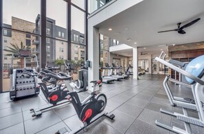 A gym with various exercise equipment, large windows, and a view of the surrounding buildings. - Enjoyable apartment in quaint Addison with fitness room access (Addison)