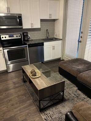 A modern kitchen with stainless steel appliances, white cabinetry, and a glass-top coffee table. - Enjoyable apartment in quaint Addison with fitness room access (Addison)