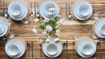 Une table à manger dressée avec de l’argenterie, de la vaisselle blanche et des verres, agrémentée d’un arrangement floral au centre.