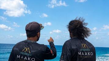 Deux personnes portant des t-shirts à manches longues noirs de la marque Maako Retreats, debout au bord de l’océan, sous un ciel dégagé.