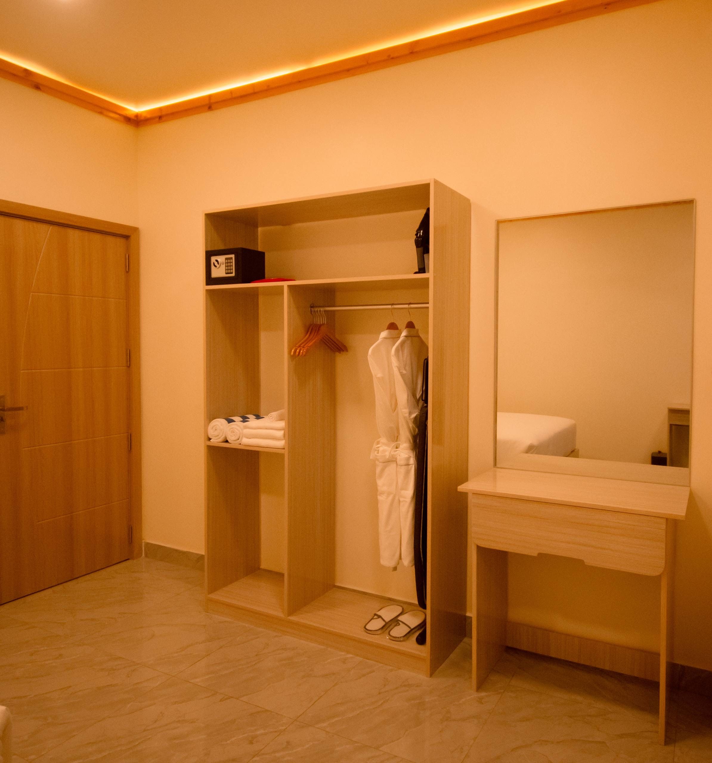 A hotel room with a wooden wardrobe, a mirror, and a bedside table.