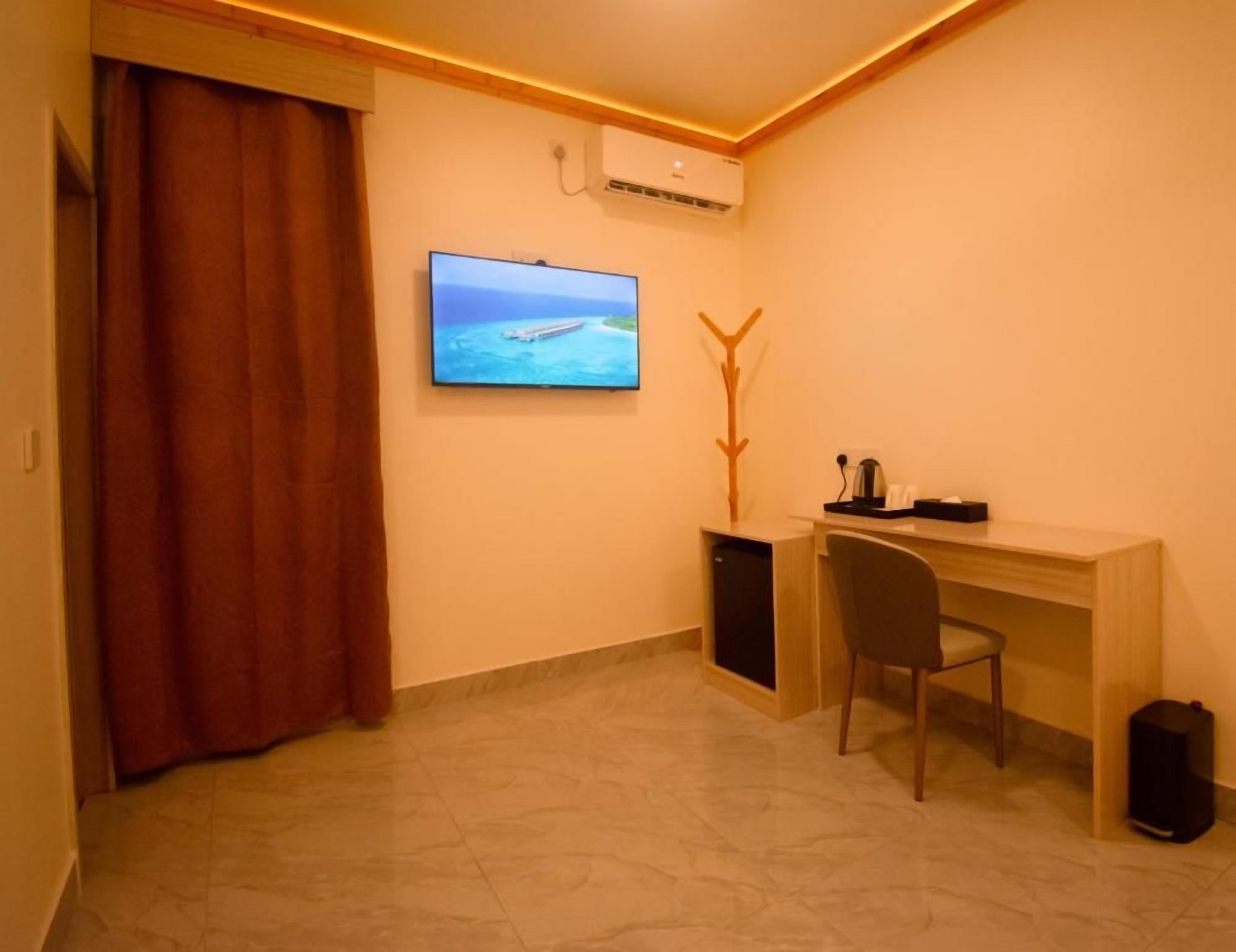 Une pièce avec un téléviseur fixé au mur, un bureau avec une chaise et un petit meuble de rangement.