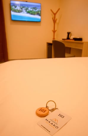 A hotel room with a bed, a television mounted on the wall, a desk with a chair, and a keychain with a number tag.