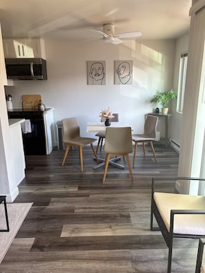 A modern kitchen with a microwave, cabinets, and a ceiling fan. There is a dining area with a table and chairs, and artwork on the wall. - Tuk on The Hill (Tukwila)