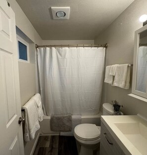 A bathroom with a shower curtain, a toilet, a sink, and a towel rack. - Tuk on The Hill (Tukwila)
