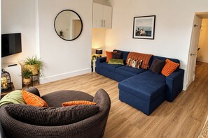 Ein Wohnzimmer mit einem blauen Sofa, einem runden Spiegel und einem Fernseher.