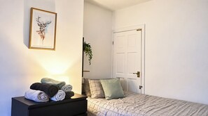 Een slaapkamer met een bed, een nachtkastje met handdoeken, een deur en een wandplant.