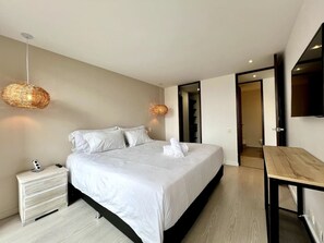 A modern bedroom with a large bed, bedside tables, a desk, and a hanging light fixture. - Premium Extended Stay Comfort Location (Medellín)