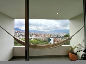 A balcony with a view of a cityscape and mountains, a hammock, and a potted plant. - Premium Extended Stay Comfort Location (Medellín)