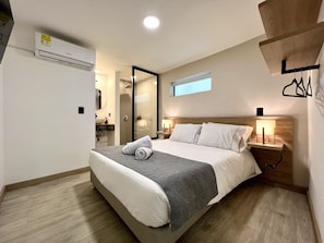 Ein Hotelzimmer mit Bett, Nachttischlampen, einem Fenster und einem durchgegangenen Türsinn erreichbarem Badezimmer.