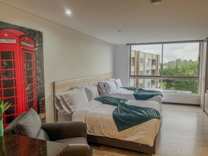 A hotel room with two beds, a red telephone booth artwork, a large window with a city view, and a small table with a plant. - Llanogrande 1BR Suite Near MDE Airport AC (Rionegro)