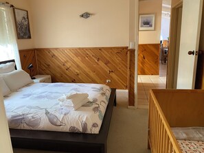 Une chambre à coucher avec une tête de lit en bois, un lit recouvert d’une literie à motifs floraux, une lampe de chevet et une petite table.