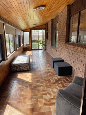 A covered patio area with a herringbone tile floor, a cushioned bench, and a seating area with a wicker table and chairs.