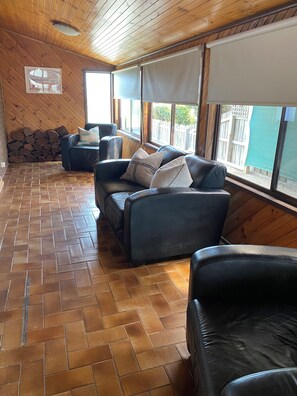 Une pièce dotée d’un parquet à motifs en chevrons, d’un mur en pierre et d’un plafond en bois. On y trouve deux canapés en cuir noir ornés de coussins à motifs.