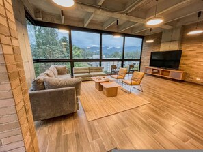 Ein modernes Wohnzimmer mit großem Fernseher, bequemen Sitzgelegenheiten und Blick ins Freie.