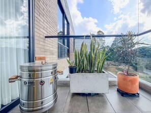 Ein Balkon mit einem Metallfass, Topfpflanzen und Blick auf die Landschaft.