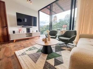 Ein modernes Wohnzimmer mit einem Flachbildfernseher, einem runden Couchtisch und zwei Sesseln.