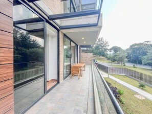 A modern building with large glass windows, a balcony with outdoor furniture, and a view of a road and greenery. - El Retiro Deluxe Apartment Parking Forest View (Retiro)