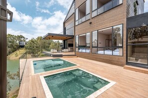 Ein modernes Haus mit zwei Außenpools, einer überdachten Terrasse und Blick auf die umliegende Landschaft.