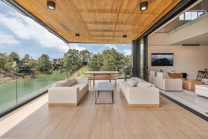 Ein modernes Wohnzimmer mit Holzboden, großen Fenstern und Blick auf einen See sowie Gebäude.