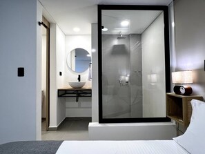 Ein modernes Badezimmer mit einer gläsernen Dusche, einem runden Spiegel und einem Nachttisch mit Lampe.