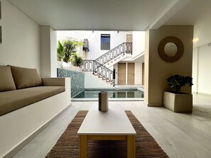 Ein modernes Wohnzimmer mit einer Couch, einem Couchtisch und Blick auf einen Pool sowie Treppen zu einer zweiten Etage.