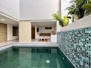 Ein moderner Poolbereich im Innenbereich mit freier Sicht auf einen Wohnbereich, inklusive einer Couch und einem Couchtisch.