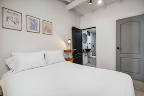 Ein Hotelzimmer mit Bett, Nachttisch, Lampe und einer Tür zu einem Badezimmer.