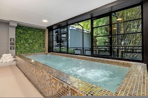 A modern indoor swimming pool with a glass bottom, surrounded by a tiled border and a green wall. - Clean Design Prime Area Effortless Stay Poblado (Medellín)