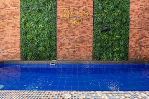 Una piscina con muro de ladrillo y follaje verde.