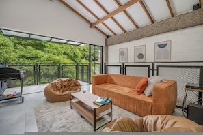 Ein modernes Wohnzimmer mit einer Couch, einem Sitzsack und einem Couchtisch. Ein Balkon bietet Blick auf Grünflächen.