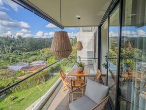 A balcony with a table and chairs, a hanging light fixture, and a view of a green landscape. - Modern Apartment El Retiro Forest View (Retiro)