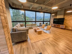Ein modernes Wohnzimmer mit großem Fernseher, bequemen Sitzmöglichkeiten und Blick ins Freie.