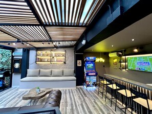 Eine Bar mit einer Nintendo-Spielstation, einer Theke und einer Sitzecke mit einer Couch und Sesseln.