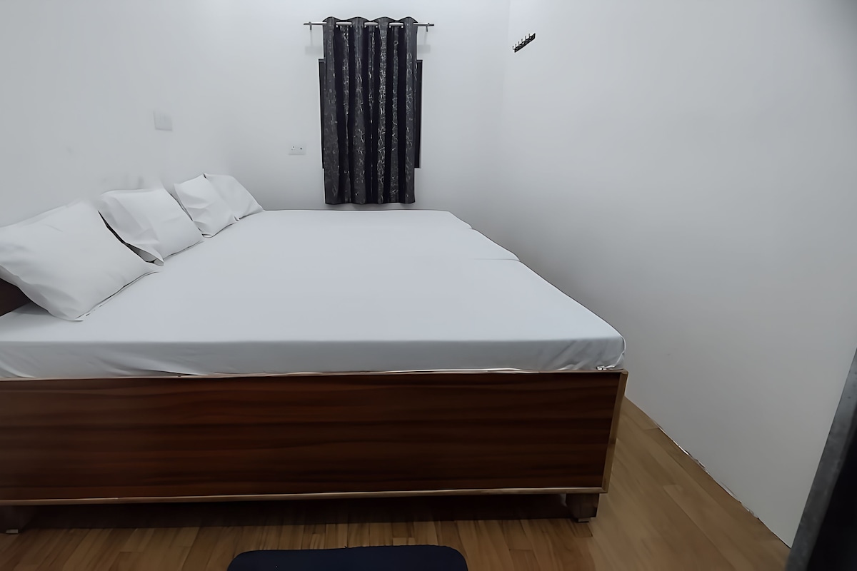 A single bed with a wooden frame and white bedding in a room with white walls and a wooden floor.