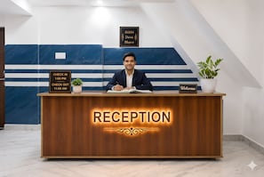 A reception desk with a sign indicating check-in and check-out times, a welcome sign, and a decorative plant. - The Kashi Vibe Homestay (Varanasi)