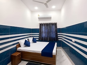 A bedroom with a bed, a nightstand, a ceiling fan, and an air conditioning unit. - The Kashi Vibe Homestay (Varanasi)