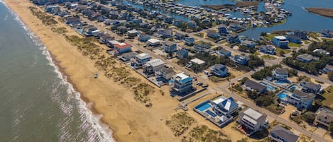 Vista aèria d'una zona residencial a la costa, amb cases, una platja i un port esportiu.