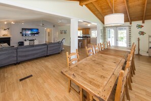 A spacious living area with a large wooden dining table, grey sofas, and a kitchen in the background. - Carefree - 5 BR north end home with Lake Tecumseh access (Virginia Beach)