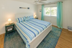 A bedroom with a bed, two bedside tables, a ceiling fan, a window with curtains, and a view of greenery outside. - Carefree - 5 BR north end home with Lake Tecumseh access (Virginia Beach)