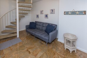 Eine Treppe mit einem Teppichpodest, ein graues Sofa mit zwei Kissen, ein kleiner Korbstuhl und Wandkunst, darunter ein Seepferdchen und ein Seestern.