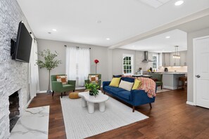 A modern living room with a fireplace, a blue sofa, and a kitchen in the background. - NEW 1-bedroom suite near BoA Stadium (Charlotte)