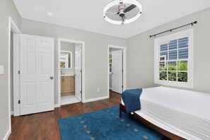 A bedroom with a bed, a ceiling fan, a window with blinds, and a door leading to a bathroom.