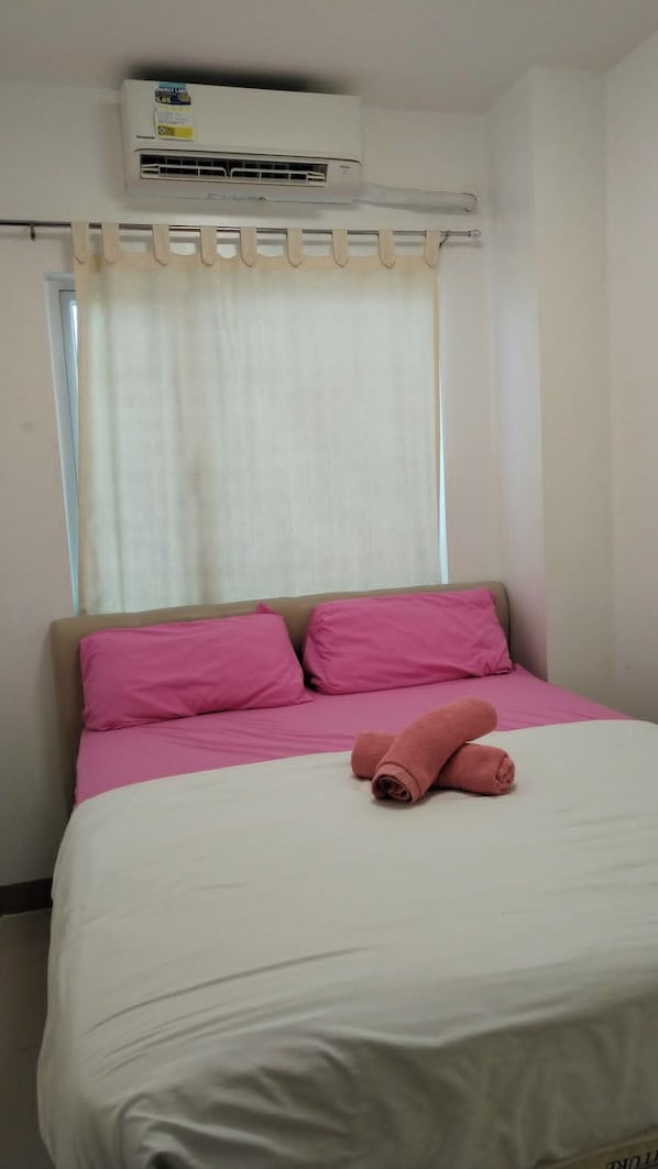 A hotel room with a bed, a window with curtains, and an air conditioning unit on the wall.