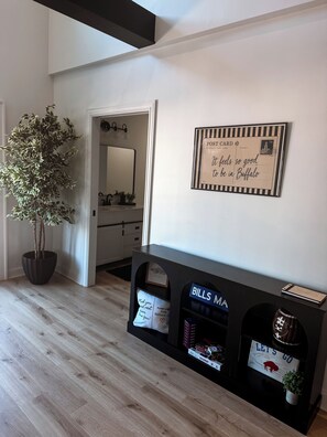 A modern interior with a wooden floor, a potted plant, a mirror, a post card, and a Bills MA sign.